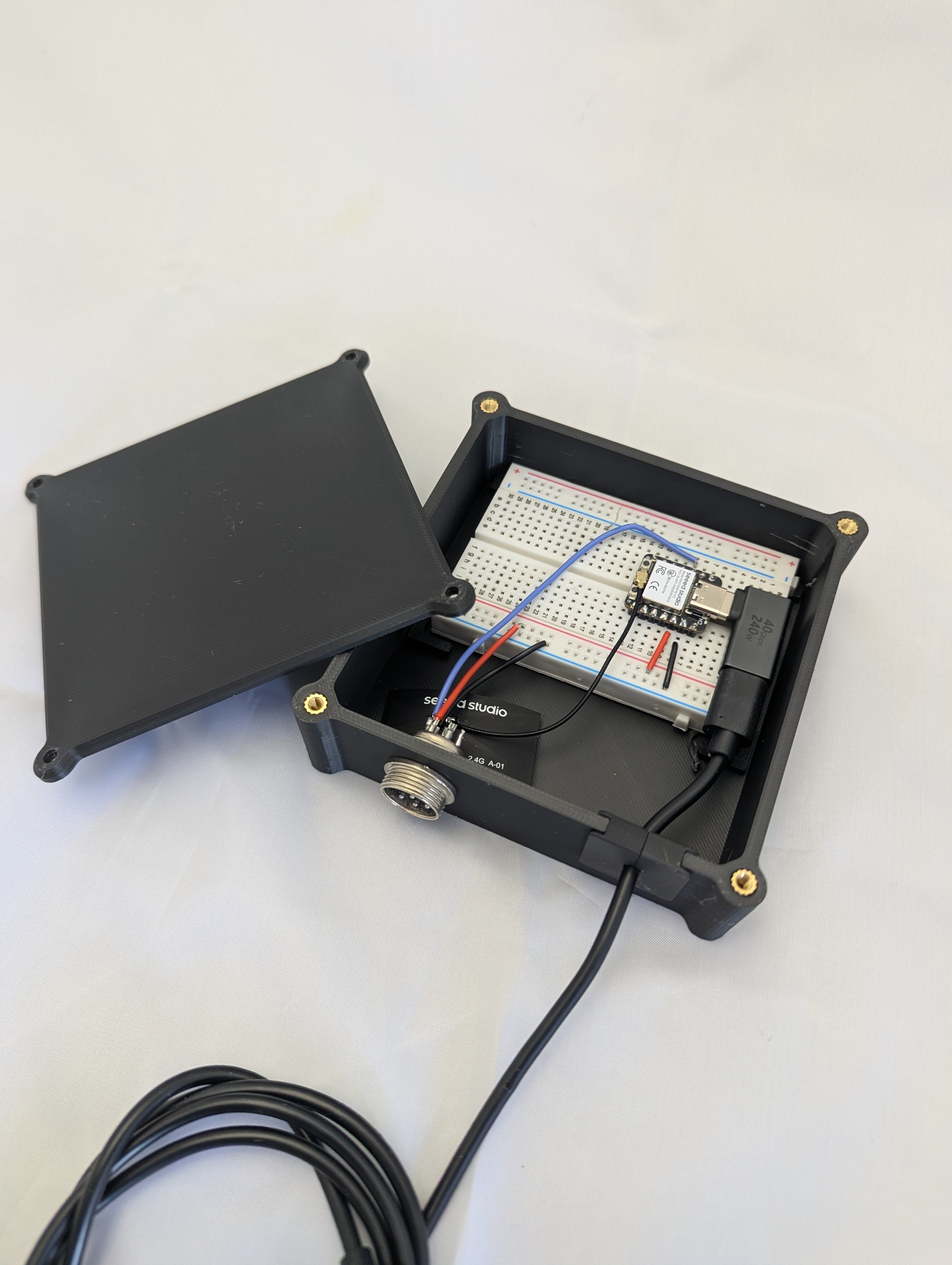 A breadboard with microcontroller housed in a black electronics enclosure with a side mounted connector and USB cable strain relief.